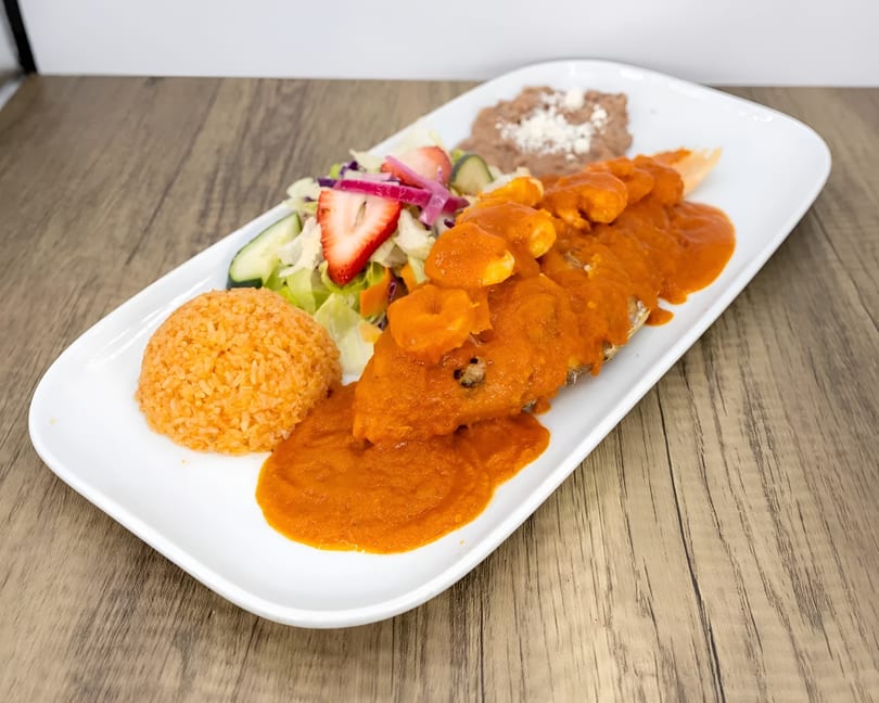 A Mexican dish with a whole fish covered in red sauce and shrimp, rice, beans, and salad.
