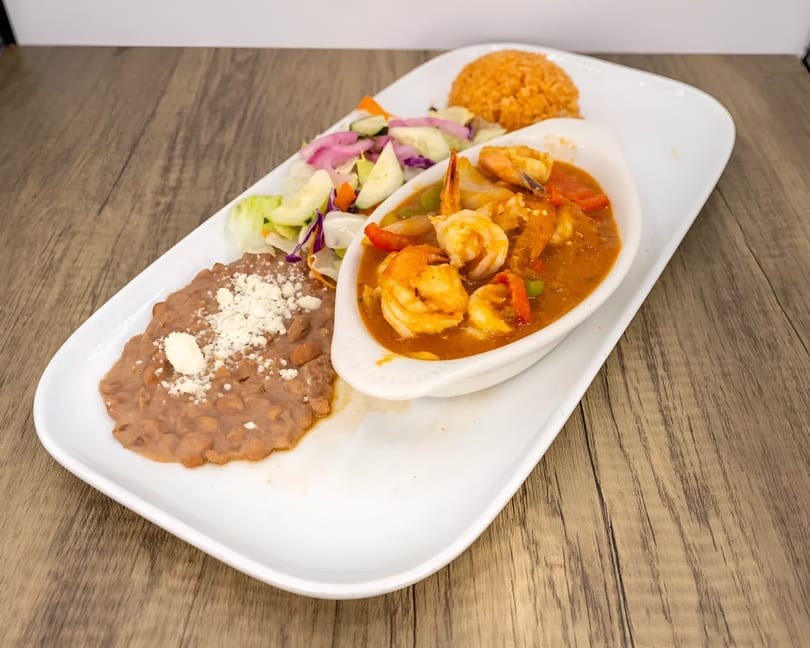 Shrimp in red sauce with rice, refried beans, and a side salad on a white rectangular plate.