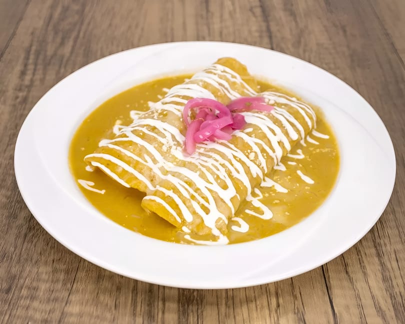 Two enchiladas covered in green sauce, drizzled with sour cream, and topped with pickled red onions.